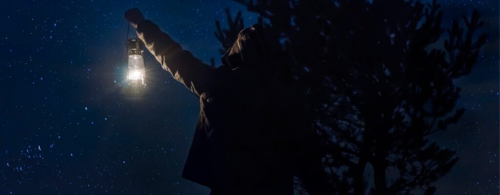 A person holds up a lantern in the dark, symbolizing the work that Four Lights Financial Advisors does helping clients find their financial way.
